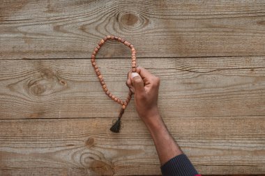 cropped shot of african american man holding beads on wooden table clipart