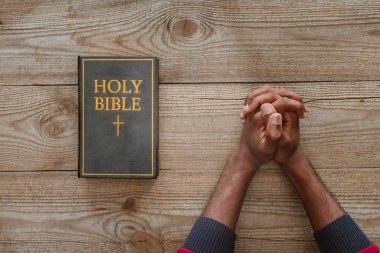 cropped shot of african american man sitting at rustic wooden table with holy bible clipart