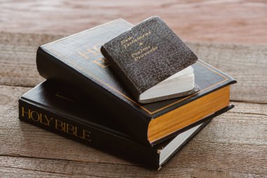 close-up shot of stacked holy bibles with new testament book on wooden surface clipart