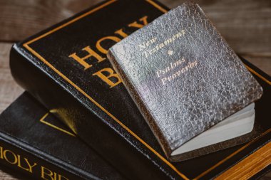 close-up shot of stacked holy bibles with new testament book on wooden tabletop clipart