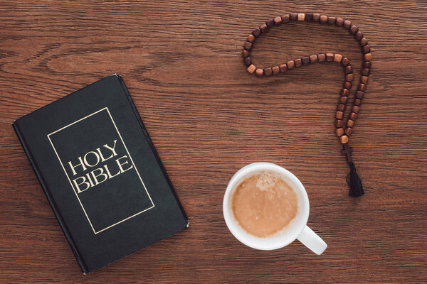 top view of holy bible with beads and coffee on wooden table