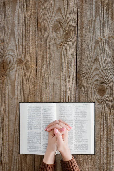 cropped shot of woman praying with holy bible on wooden table