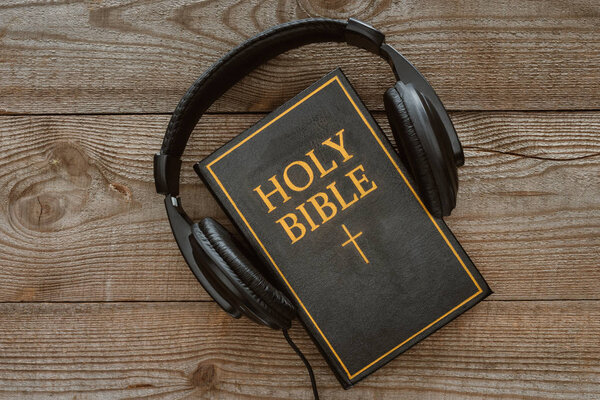 top view of holy bible with headphones on wooden tabletop