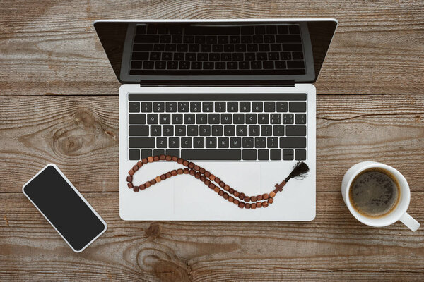 top view of laptop and smartphone with beads and coffee on wooden table