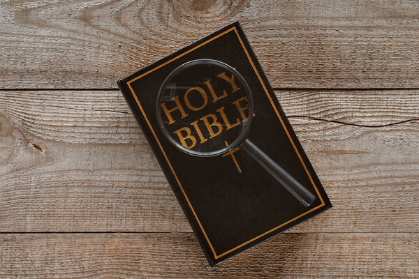 верхний вид на святую Библию с лупой на деревянном столе
