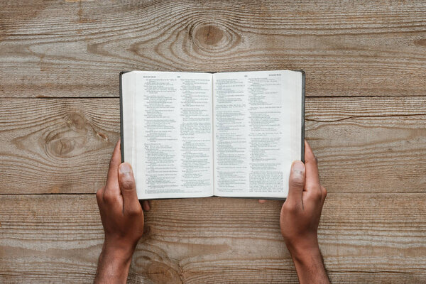 cropped shot of man holding holy bible over wooden table