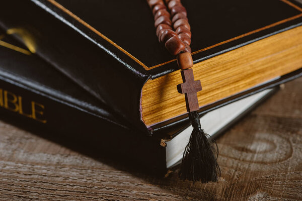close-up shot of stacked holy bibles with beads on wooden table