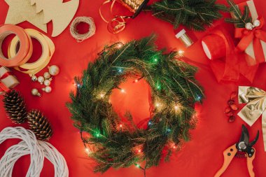 çam ağacı dalları, Noel ışıkları ve şeritleri için el yapımı Noel çelenk kırmızı zemin üzerinde düz lay