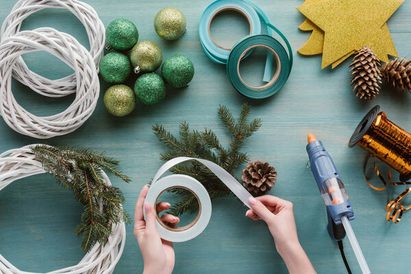 частичный вид женщины, держащей ленту для украшения венков ручной работы на голубой деревянной поверхности
