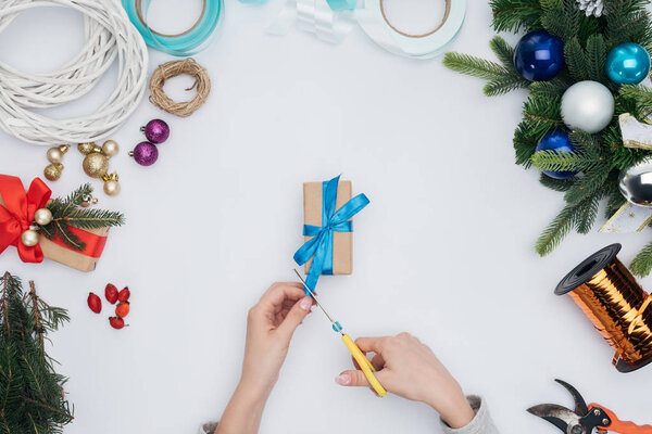 partial view of woman cutting blue ribbon on wrapped christmas present isolated on white