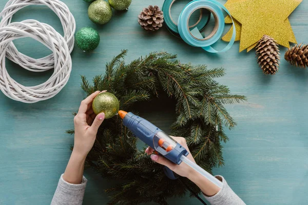 Partial view of woman decorating handmade pine tree wreath with christmas toys on blue wooden surface — Stock Image Partial View Woman Decorating Handmade Pine Tree Wreath Christmas Toys Stock Picture