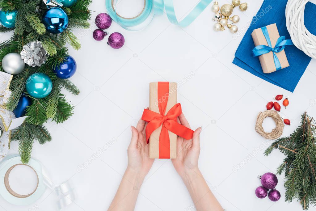 partial view of woman holding wrapped christmas gift with red ribbon isolated on white