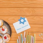 Posa piatta con ciambelle, candele, menorah e felice carta hannukah sulla superficie di legno, concetto di hannukah