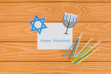 flat lay with happy hannukah card, candles and paper holiday signs on wooden tabletop, hannukah concept clipart