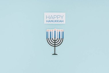 top view of happy hannukah card and paper menirah sign isolated on blue, hannukah concept clipart