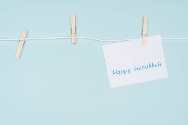 top view of happy hannukah card pegged on rope with clothes peg isolated on blue, hannukah concept clipart