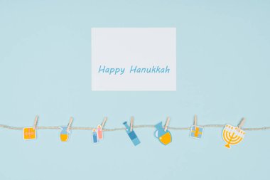 top view of happy hannukah card and holiday paper signs pegged on rope isolated on blue, hannukah concept clipart