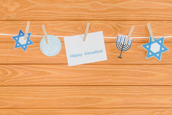top view of happy hannukah card and holiday paper signs pegged on rope on wooden tabletop, hannukah concept
