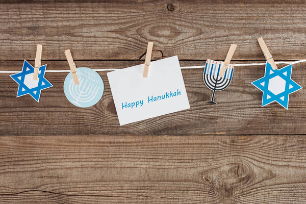 top view of happy hannukah card and holiday paper signs pegged on rope on wooden tabletop, hannukah concept