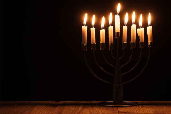 close up view of jewish menorah with candles for hannukah holiday celebration on wooden surface on black backdrop, hannukah concept