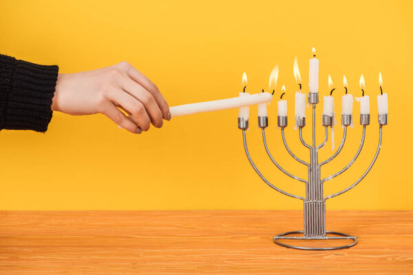 partial view of woman lighting candles on menorah isolated on yellow, hannukah holiday concept