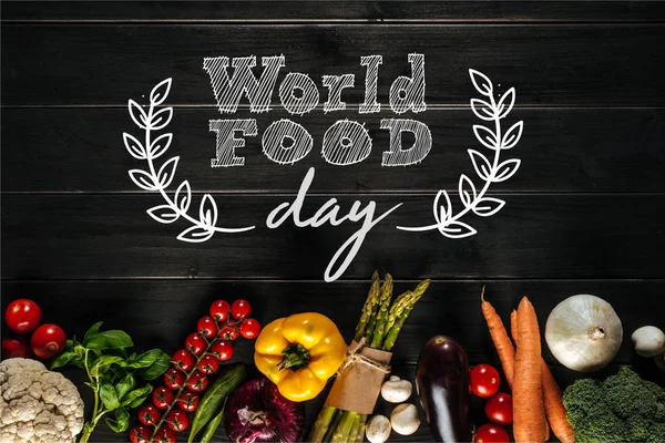 世界の食糧日碑文と木製のテーブルの上の行の横になっているさまざまな新鮮な野菜 — ストック写真