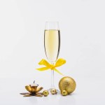 Close up view of glass of champagne, decorative candle and christmas balls on white backdrop