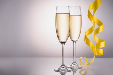 close up view of glasses of champagne and yellow festive confetti on grey background