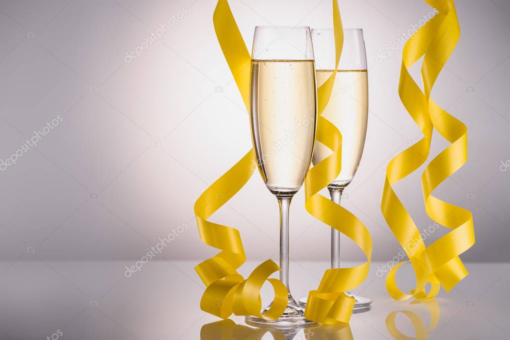 close up view of glasses of champagne and yellow festive confetti on grey background