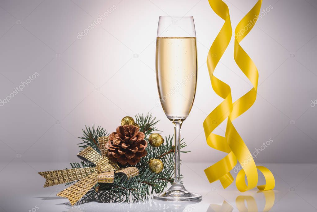 close up view of glass of champagne, christmas decoration and confetti on grey backdrop