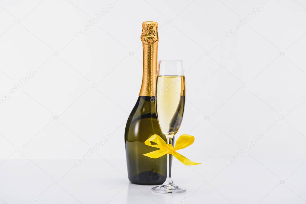 close up view of bottle and glass of champagne with yellow ribbon on white backdrop 