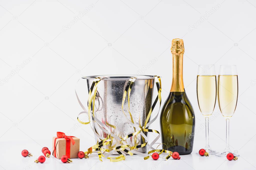 close up view of bottle of champagne, bucket with confetti, glasses of champagne and wrapped christmas gift on grey background