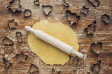 flat lay with raw dough, rolling pin and cookie cutters arranged on wooden tabletop clipart