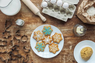 düz lay Noel kurabiyeleri plaka, malzemeler ve ahşap masa üzerinde düzenlenmiş çerez kesici ile