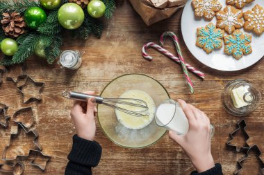 kadın dökülen süt kırpılmış atış dekoratif çelenk ile ahşap masa üzerinde Noel kurabiyeleri için hamur yaparken kasenin içine