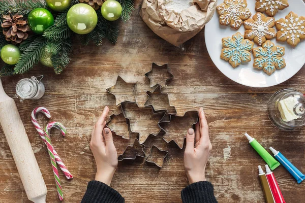 木製卓上のクリスマス クッキーと焼きたてのクッキーのカッターを保持している女性の部分的なビュー — ストック写真