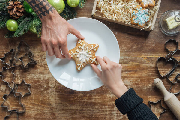 partial view of man and woman holding homemade cookie on wooden tabletop with decorative christmas wreath