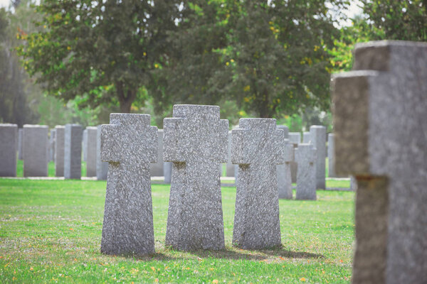 selective focus of identical old gravestones placed in row on grass at cemetery