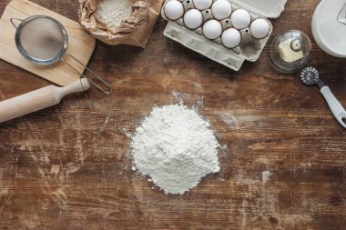 top view of white flour pile and baking ingredients on wooden table clipart
