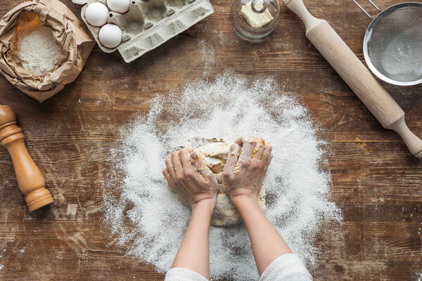 top view of female hands making dough on wooden table