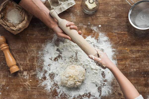 top view of cookers hands holding rolling pin above wooden table