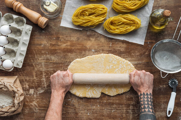 top view of male hands forming dough with rolling pin on wooden table