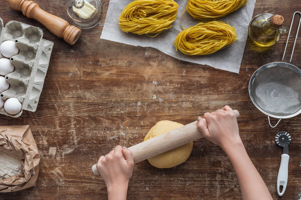 top view of female hands rolling out dough on wooden table