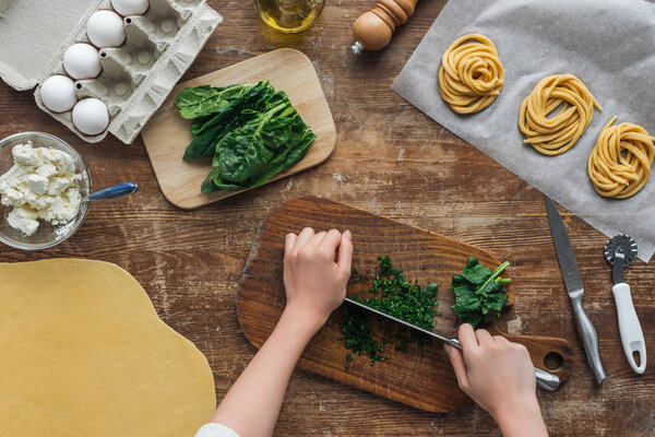 top view of female hands cutting spinach on wooden chopping board