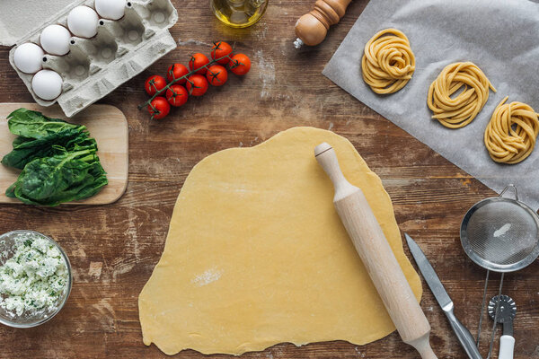 top view of raw dough with rolling pin and pasta ingredients on wooden table