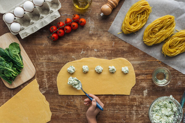 top view of female hands putting creamy cheese filling on dough for ravioli at wooden table