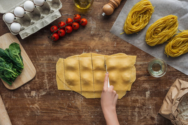 top view of female hands cutting out ravioli at wooden table