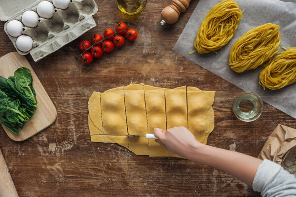 top view of female hands cutting out ravioli at wooden table