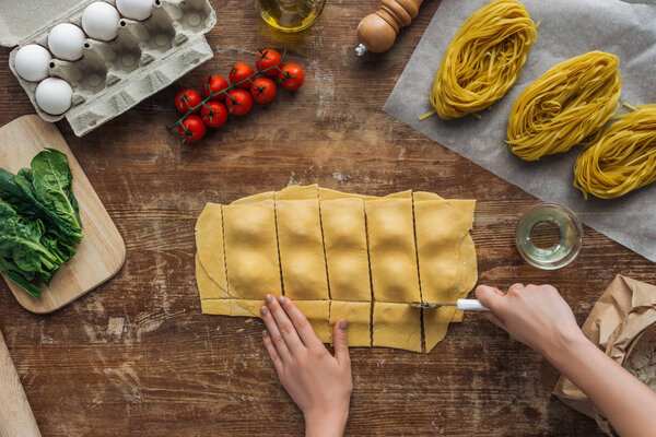 top view of female hands cutting out ravioli with pastry wheel at wooden table