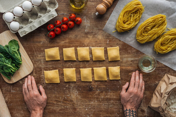 top view of male hands and raw ravioli at wooden table